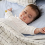 Smiling baby girl lying on a bed sleeping on blue sheets